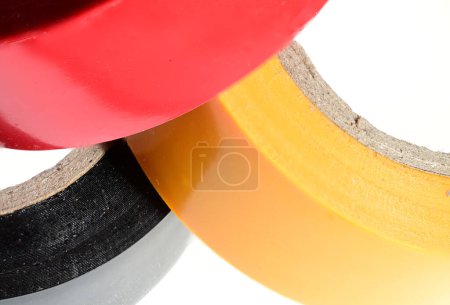 Foto de Vista parcial de cerca extrema de tres rollos rojos negros amarillos multicolores apilados de cinta adhesiva cinta adhesiva sobre fondo blanco como concepto para aislar contactos eléctricos - Imagen libre de derechos
