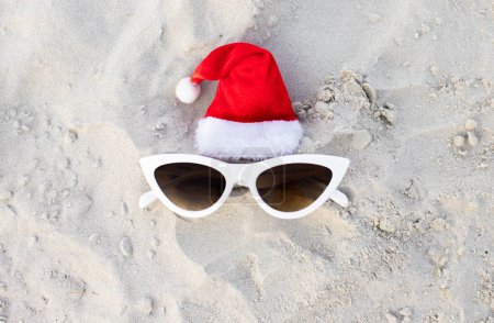 Photo for Christmas background. Santa Claus hat on the beach with sunglases.Christmas card and advent calendar concept. Travel ticket sale concept for christmas holidays.Copy space.Top view photo.High quality - Royalty Free Image