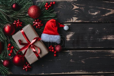 Foto de Foto vista superior Caja de regalo de Navidad flatlay, juguetes de árbol de Navidad rojo, sombrero de Santa y brance de abeto sobre fondo de madera. Fondo de Navidad con espacio para text.Copyspace. - Imagen libre de derechos