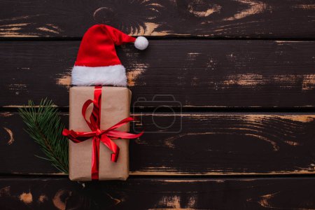 Photo for Top view photo christmass flatlay gift box,Santa hat and christmas spruce branch on wooden background. Xmas backdrop with space for text.Copyspace. - Royalty Free Image