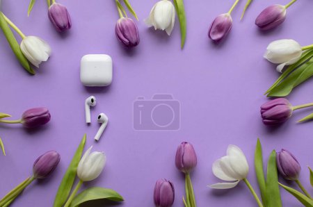 Téléchargez les photos : Wireless headphones pods and Spring tulips on violet background.Top view photo.Copy space. - en image libre de droit