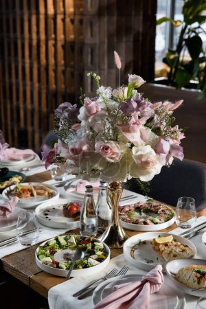 Foto de Mesa servida en el restaurante está decorado con un ramo de lujo. Rosas de jardín, eustoma, eucalipto populus. colores pastel. - Imagen libre de derechos