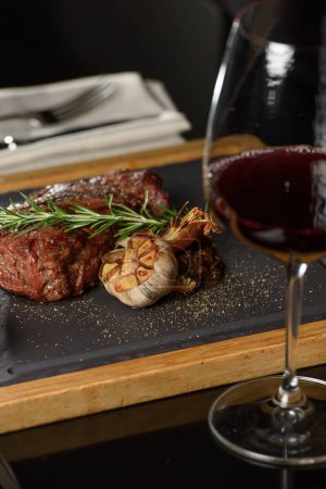 Succulent grilled beef steak with red wine, seasonings, fresh rosemary and grilled vegetables on cutting board.