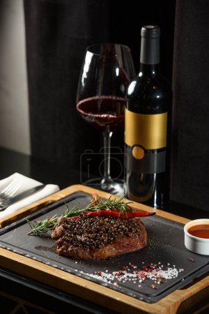 Succulent grilled beef steak with red wine, seasonings, fresh rosemary and grilled vegetables on cutting board.
