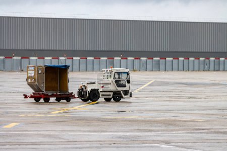 Photo for Aeroport Charles de Gaulle, France October 24, 2023: White Tug Vehicle Towing Luggage Cart on Tarmac - Royalty Free Image