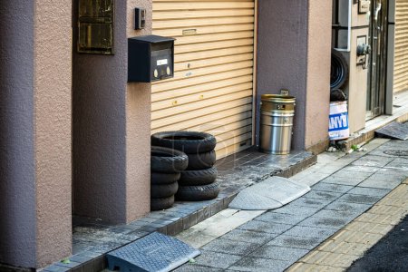 Foto de Tokio, Japón, 26 de octubre de 2023: Neumáticos apilados y papelera junto a un edificio residencial - Imagen libre de derechos