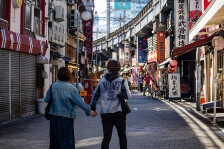 Téléchargez les photos : Tokyo, Japon, 26 Octobre 2023 : Couple marchant main dans la main dans une allée commerçante - en image libre de droit