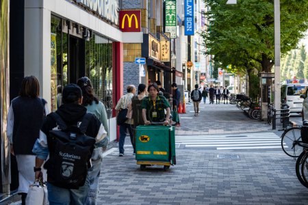 Téléchargez les photos : Tokyo, Japon, 26 octobre 2023 : Un livreur dans une rue animée de Tokyo avec des acheteurs et des cyclistes. - en image libre de droit