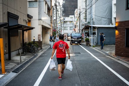 Foto de Tokio, Japón, 28 de octubre de 2023: Hombre caminando por el callejón llevando comestibles - Imagen libre de derechos