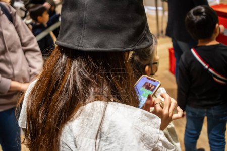 Photo for Tokyo, Japan, 29 October 2023 : Young customer playing a handheld game in a crowded store - Royalty Free Image