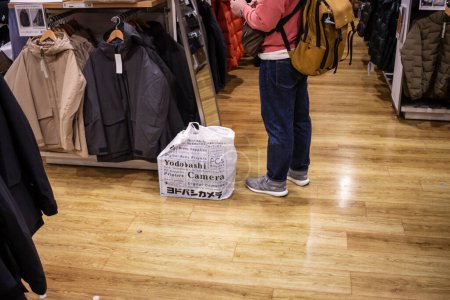 Foto de Tokio, Japón, 30 de octubre de 2023: Cliente con bolsa de compras mirando abrigos en una tienda minorista - Imagen libre de derechos