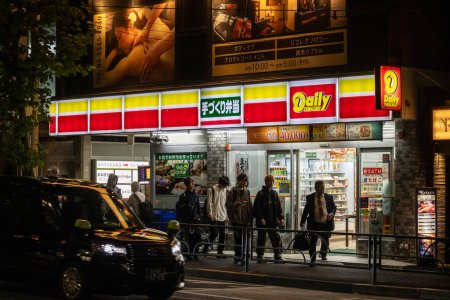 Photo for Tokyo, Japan, 31 October 2023: Brightly lit Daily Yamazaki convenience store at night with customers - Royalty Free Image