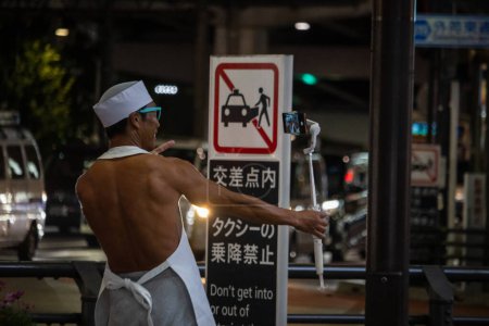 Téléchargez les photos : Tokyo, Japon, 31 octobre 2023 : Un chef torse nu prend un selfie devant un panneau d'interdiction de stationnement - en image libre de droit