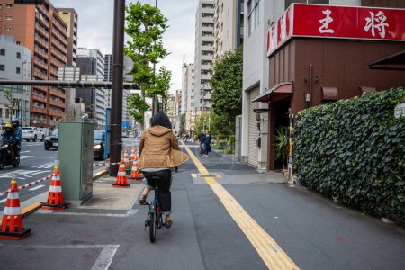 Téléchargez les photos : Tokyo, Japon, 31 octobre 2023 : Cycliste sur une piste cyclable à Tokyo avec des cônes de construction et un panneau de restaurant - en image libre de droit