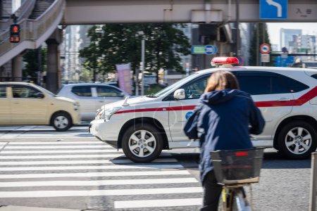 Photo for Tokyo, Japan, 1 November 2023: Cyclist Waiting at Pedestrian Crossing with Police Car in Background - Royalty Free Image