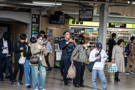 Téléchargez les photos : Tokyo, Japon, 1 Novembre 2023 : Les navetteurs attendent et utilisent des téléphones intelligents sur une plate-forme de gare occupée - en image libre de droit