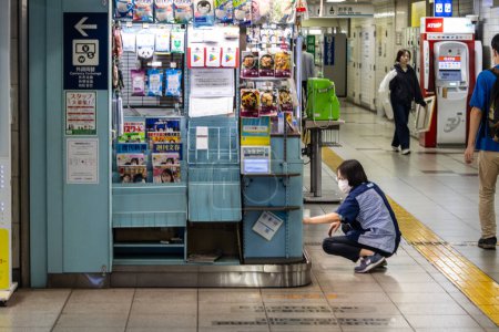 Foto de Tokio, Japón, 2 de noviembre de 2023: Obrero organizando revistas en un quiosco de la estación de metro - Imagen libre de derechos