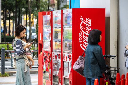 Téléchargez les photos : Tokyo, Japon, 2 Novembre 2023 : Femme utilisant un smartphone par Coca-Cola distributeurs automatiques - en image libre de droit