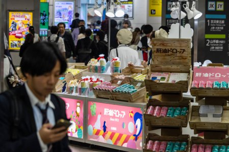 Téléchargez les photos : Tokyo, Japon, 2 novembre 2023 : Un homme utilise un smartphone devant un stand de cosmétiques colorés - en image libre de droit