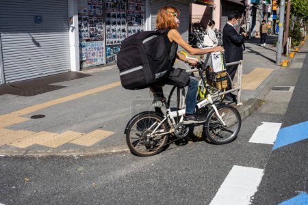 Téléchargez les photos : Tokyo, Japon, 2 novembre 2023 : Femme en vélo pliant au croisement de rue avec des piétons - en image libre de droit