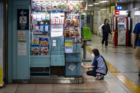 Foto de Tokio, Japón, 2 de noviembre de 2023: Persona en cuclillas frente a un quiosco de la estación de metro - Imagen libre de derechos