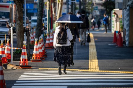 Téléchargez les photos : Tokyo, Japon, 2 novembre 2023 : Femme traversant la rue avec un parapluie à Tokyo - en image libre de droit