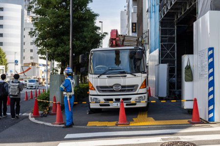 Téléchargez les photos : Tokyo, Japon, 2 novembre 2023 : Site de construction à Tokyo avec un travailleur guidant un camion - en image libre de droit