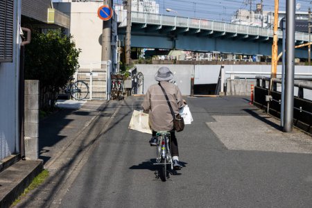 Foto de Tokio, Japón, 3 de noviembre de 2023: Personas mayores en bicicleta en una calle de la ciudad con un puente y edificios en el fondo - Imagen libre de derechos