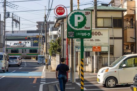 Foto de Tokio, Japón, 3 de noviembre de 2023: Hombre caminando junto a un cartel de estacionamiento con el tren en el fondo - Imagen libre de derechos