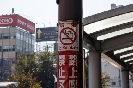 Téléchargez les photos : Tokyo, Japon, 3 Novembre 2023 : No Smoking Sign on a Street Pole with City Background - en image libre de droit