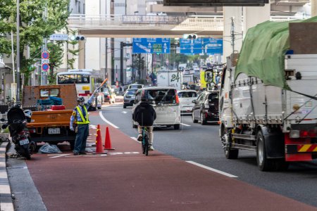 Téléchargez les photos : Tokyo, Japon, 4 Novembre 2023 : Cycliste naviguant à travers la circulation urbaine achalandée à côté de la construction routière - en image libre de droit