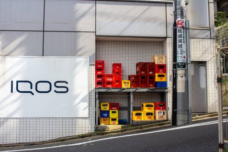 Foto de Tokio, Japón, 4 de noviembre de 2023: Cajas de bebidas coloridas apiladas por un cartel de IQOS en la calle Tokyo - Imagen libre de derechos