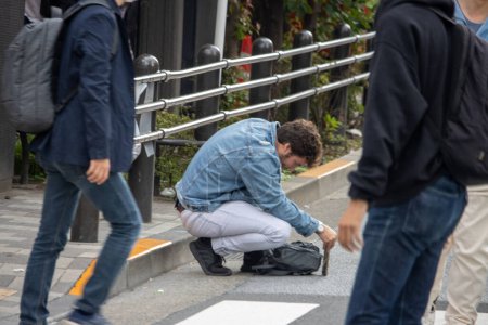 Photo for Tokyo, Japan, November 5 2023 : Man Crouching to Adjust Backpack on City Street - Royalty Free Image