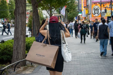 Foto de Tokio, Japón, 6 de noviembre de 2024: Mujer con bolsas de compras caminando por la calle concurrida - Imagen libre de derechos