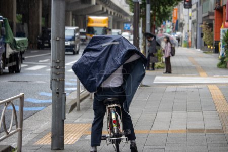 Téléchargez les photos : Tokyo, Japon, 7 Novembre 2024 : Cycliste Riding in Rain with Improvised Poncho - en image libre de droit