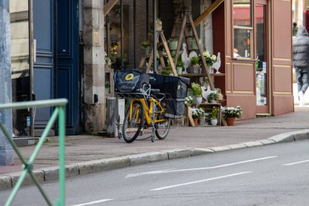 Foto de Francia, 30 de marzo de 2024: Bicicleta de reparto de servicios postales estacionada fuera de una florería - Imagen libre de derechos