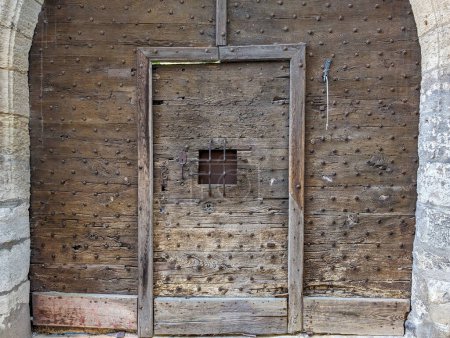 Photo for France, April 22, 2024: Ancient wooden door with metal studs and barred window in a historic building - Royalty Free Image