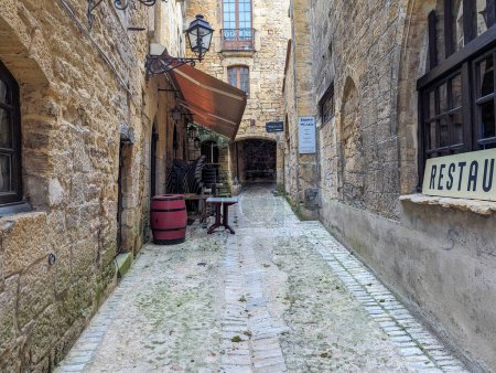 Téléchargez les photos : France, 7 avril 2024 : Une ruelle pavée étroite dans une vieille ville européenne avec des bâtiments rustiques et un panneau de restaurant - en image libre de droit