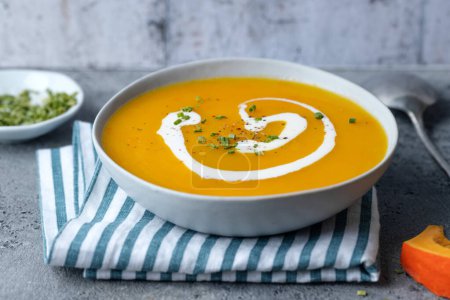 Foto de Autumnal pumpkin soup served in bowl on grey background. Closeup - Imagen libre de derechos