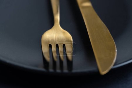 Téléchargez les photos : Golden cutlery on plate on dark background. Closeup. Eating concept. - en image libre de droit