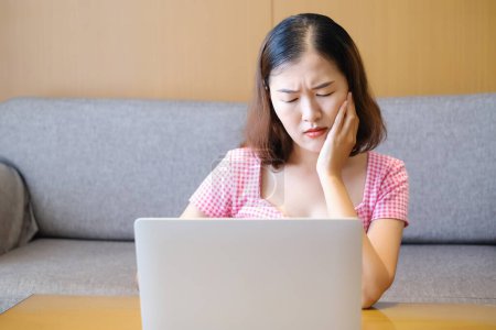 Mujer asiática dolor de cabeza porque jugar o trabajar con el ordenador portátil, trabajar desde casa