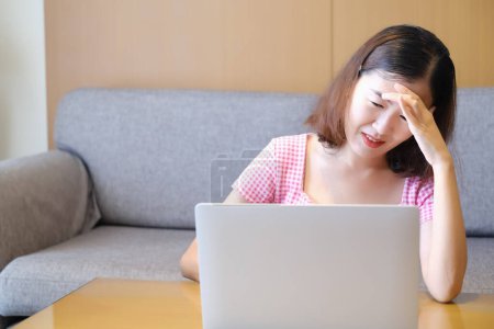 Asiatische Frau Kopfschmerzen, weil spielen oder arbeiten mit Laptop, Arbeit von zu Hause aus