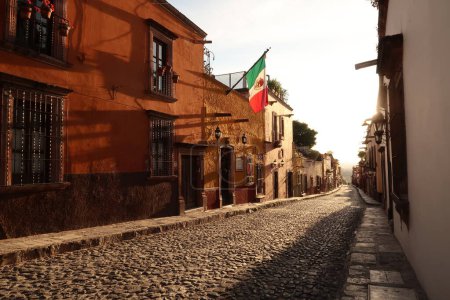 Foto de Típica calle adoquinada en San Miguel de Allende a la hora dorada / atardecer, una bandera mexicana cuelga en una fachada, México 2022 - Imagen libre de derechos