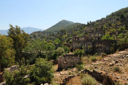 Kopfsteinpflaster führt den Hügel hinauf mit den Ruinen der verlassenen Häuser von Kayakoy im Hintergrund, in der Nähe von Fethiye, Türkei 2022
