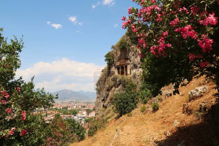 Das in Felsen gehauene antike lykische Grab des Amyntas im ehemaligen Telmessos, mit heutzutage Fethiye im Hintergrund und rosa Blumen im Vordergrund, Türkei