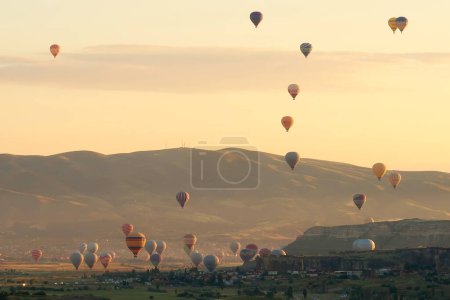 Many colorful hot air balloons over the landscape of the Red Valley, Rose Valley about to land next to Cavusin after sunrise, Cappadocia, Turkey 2022