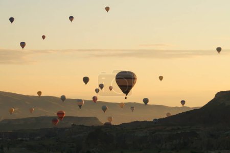 Many colorful hot air balloons over the landscape of the Red Valley, Rose Valley about to land next to Cavusin after sunrise, Cappadocia, Turkey 2022