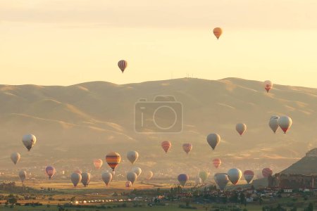Many colorful hot air balloons over the landscape of the Red Valley, Rose Valley all about to land next to Cavusin after sunrise, Cappadocia, Turkey 2022