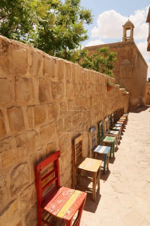 A row of colorful wooden chairs in a row in front of a wall next to the Mor Yusuf Kilisesi Church in the old town of Mardin, Turkey 2022