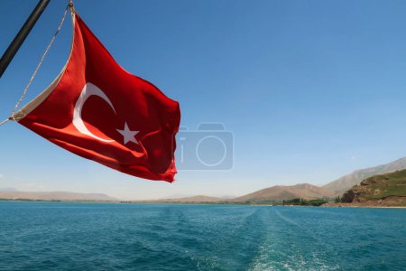 Red national flag of turkey flying, waving in the wind on the boat ride crossing Lake Van, Van Golu to Akdamar Island, close to Van, Turkey 2022